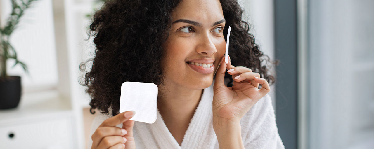 Mujer de piel rizada sonriendo mientras sostiene Pads JGB y realiza su rutina de skincare