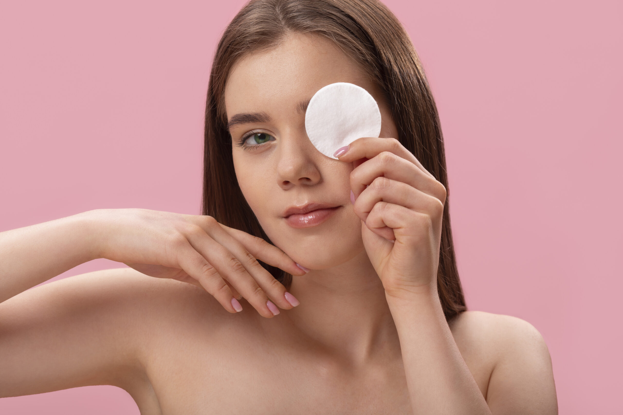Mujer sosteniendo pomos desmaquillantes de algodón sobre su rostro durante su rutina de limpieza facial.